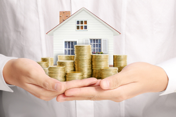 holding model house surrounded by coins